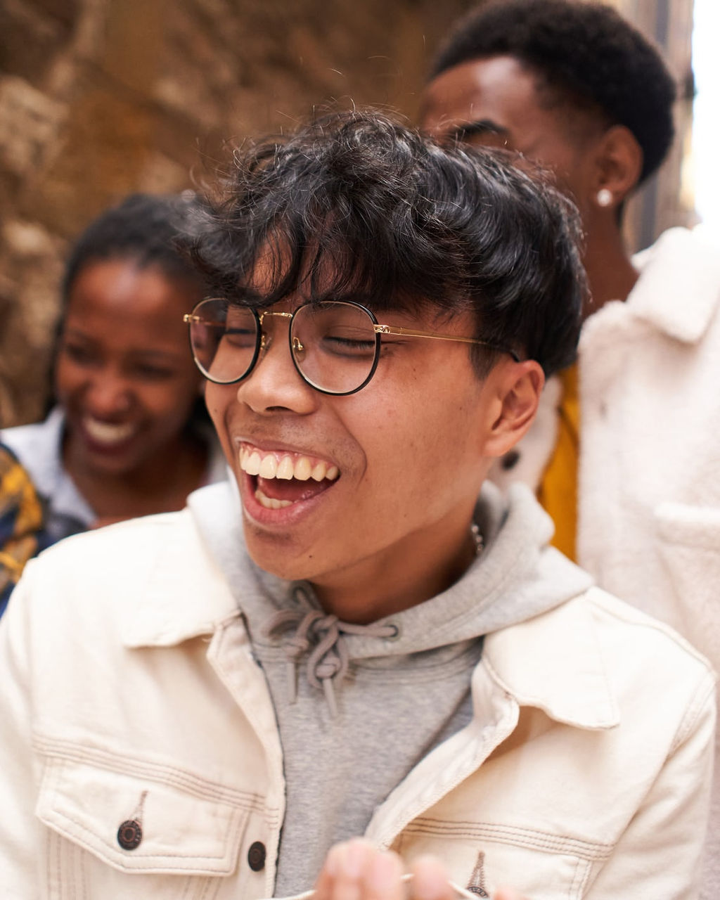 Un joven con gafas está sonriendo con otros dos jóvenes de fondo