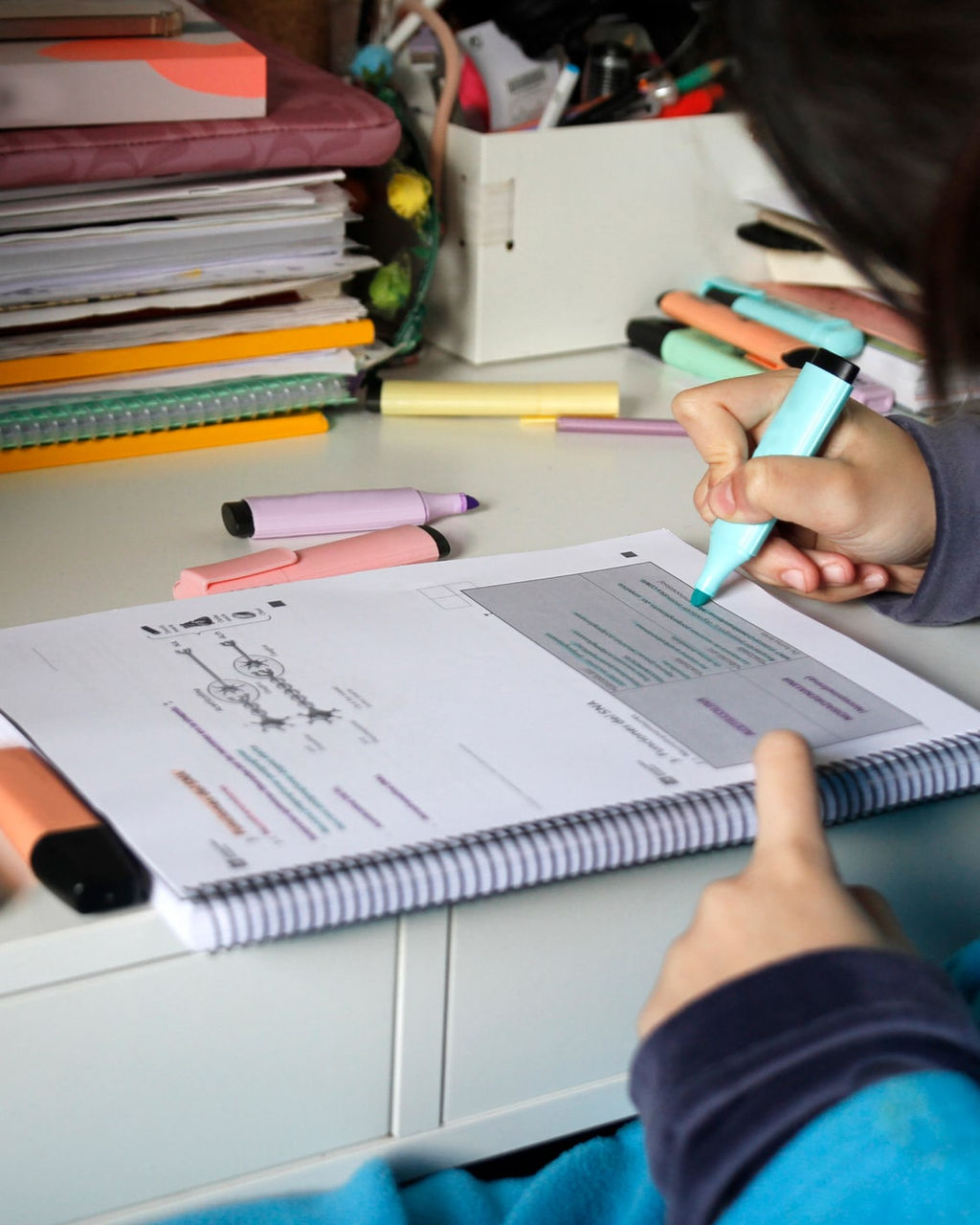 Primer plano de la mano de un estudiante, utilizando un marcador azul para resaltar texto en un cuaderno