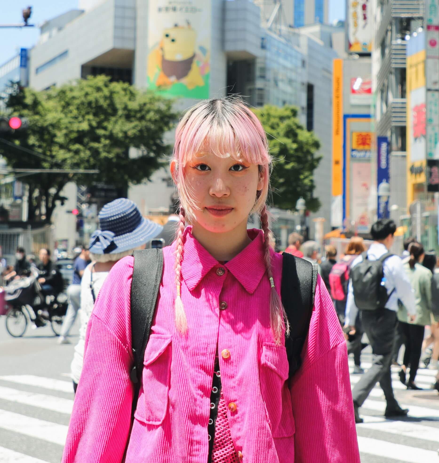 Joven con el pelo rosa y una camisa rosa está de pie en una calle concurrida de la ciudad