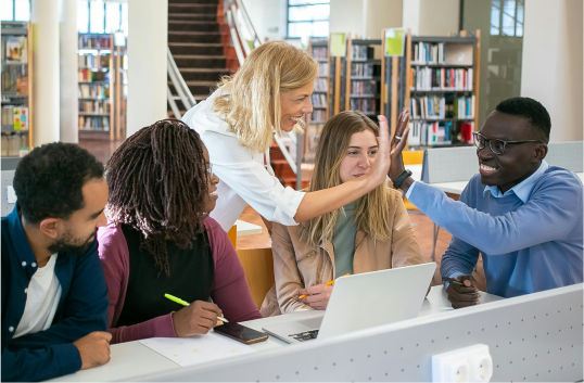A group of people looking at a laptop in a library setting.