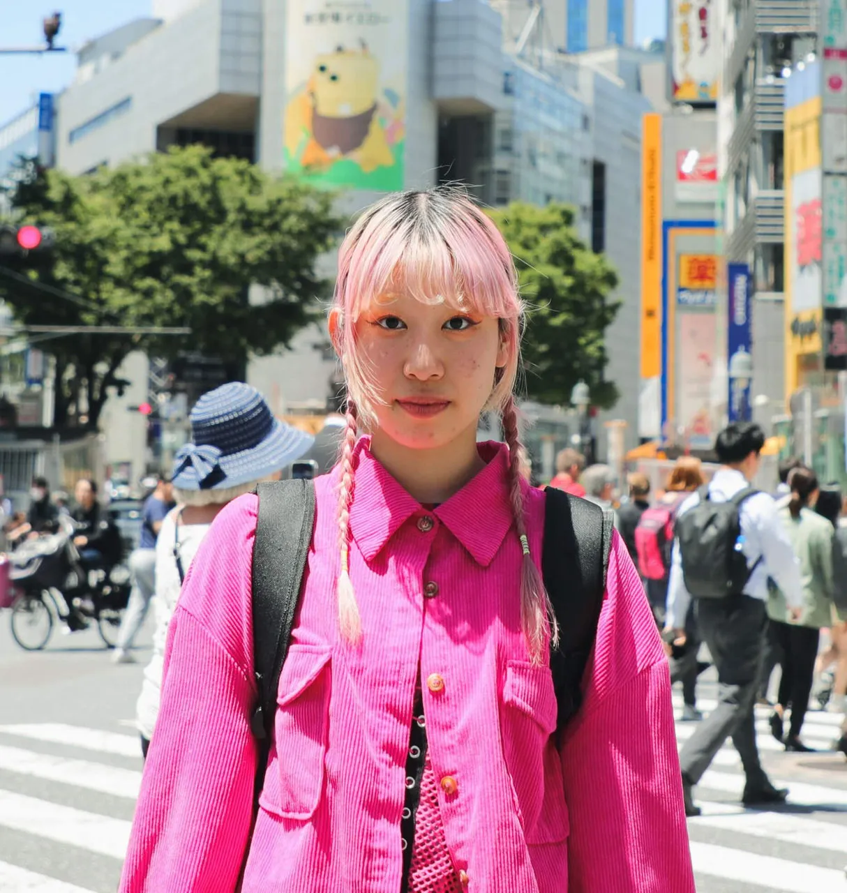 Mujer joven con cabello rosa y camisa rosa se levanta en una calle de ciudad concurrida