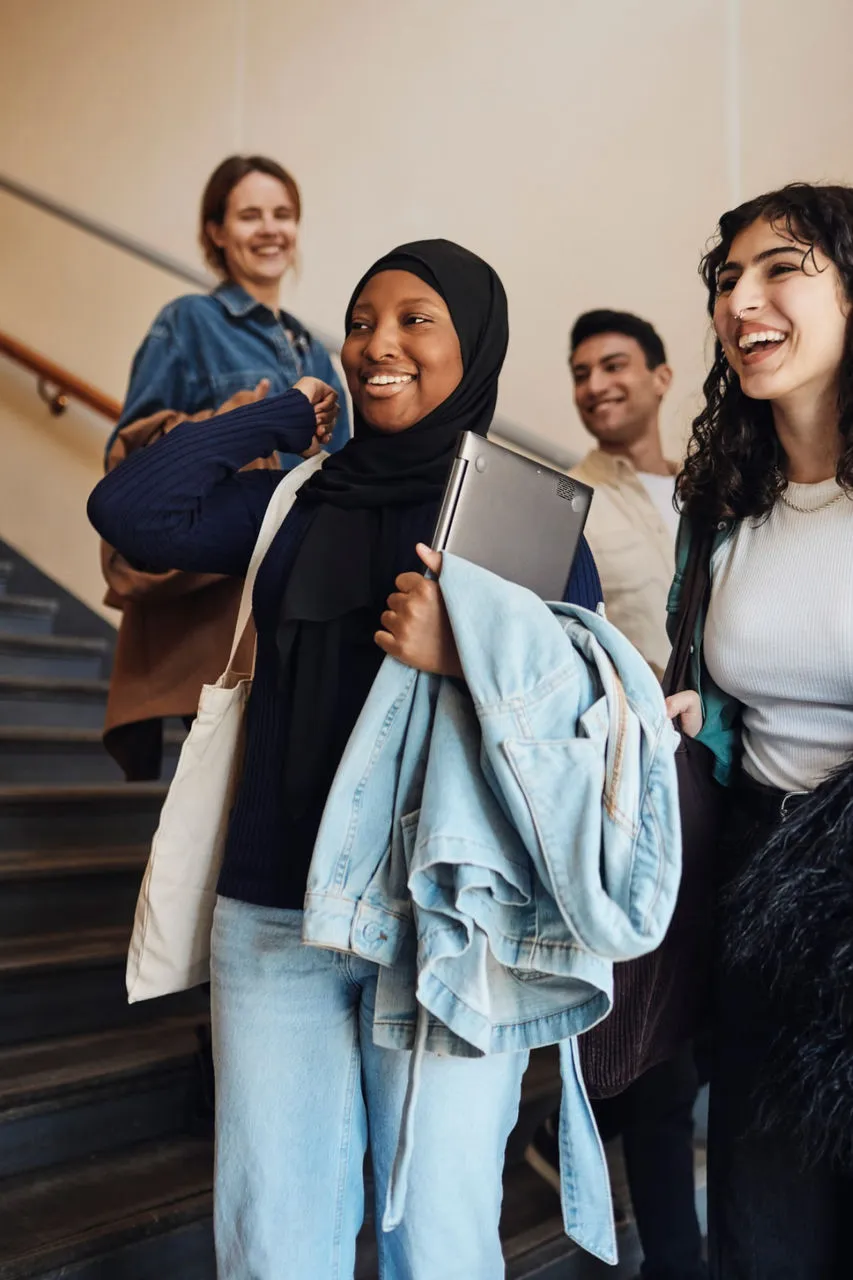 Mujer sonriente en hijab sostiene un portátil mientras baja escaleras