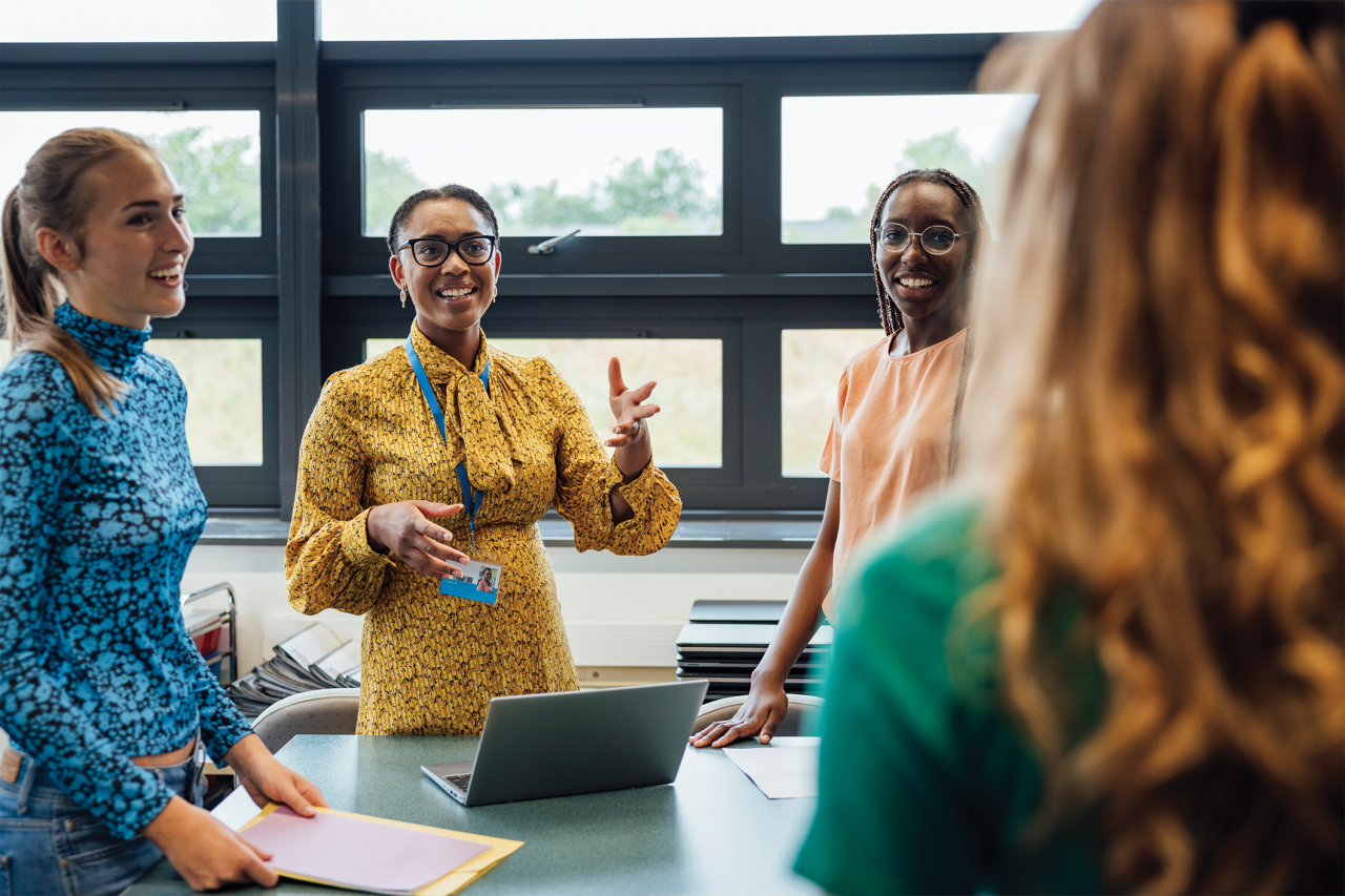 A shot of a mid-adult secondary school teacher talking with her sixth form students in class, they are wearing casual clothing and discussing what they learned in class, in a school in Gateshead, England.